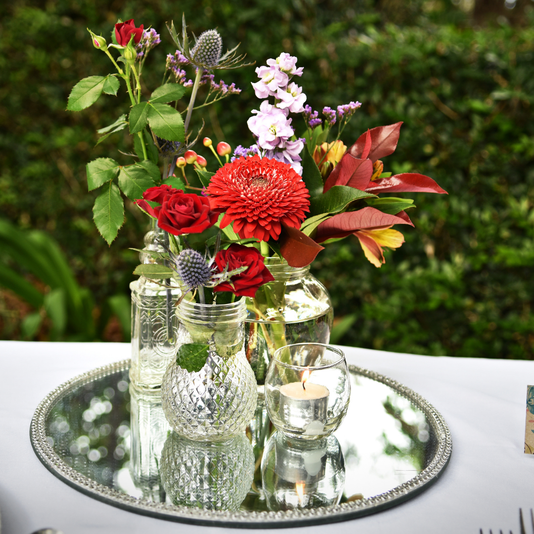 Assorted vases and mason jars on a charger plate with votive candles